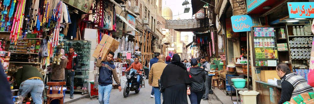 Cairo, Egypt. Busy streets in Khan el Khalili bazar shops store fronts mosque minaret people working walking by souvenirs